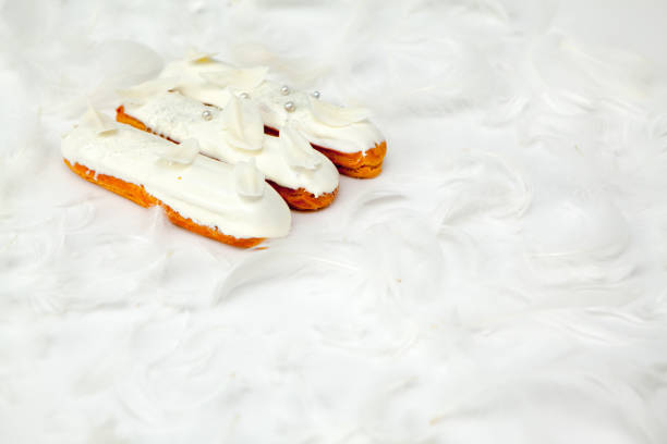 A set of three eclairs with white chocolate decor isolate on a white surface decorated with white feathers