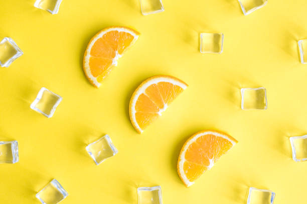 istock Top view tropical background composition made of orange fruit slices and ice cubes abstract on yellow. 1159267668