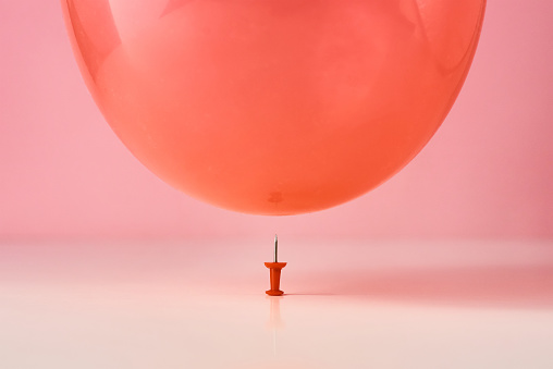 Red balloon fall on pin needle on pink background. Danger or protection concept