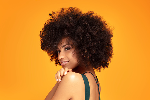 Beauty portrait of african american woman with glamour makeup and afro hairstyle posing on yellow background. Smiling happy girl.