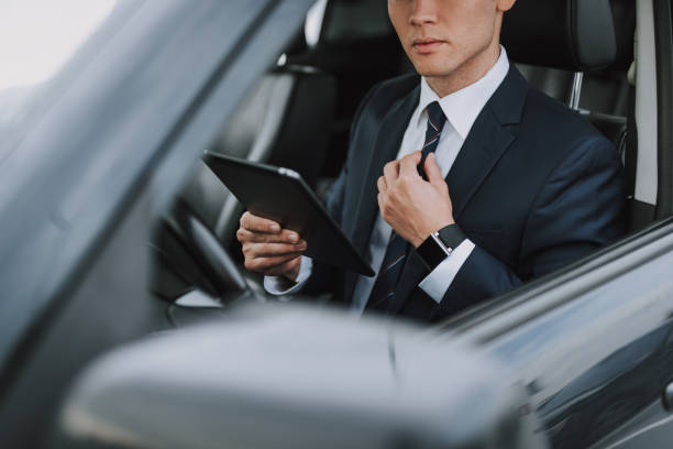 istock Young handsome guy in suit sitting in his car with tablet 1159270172