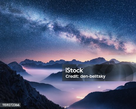 istock Milky Way over mountains in fog at night in summer. Landscape with foggy alpine mountain valley, purple low clouds, colorful starry sky with milky way, city illumination. Dolomites, Italy. Space 1159272366