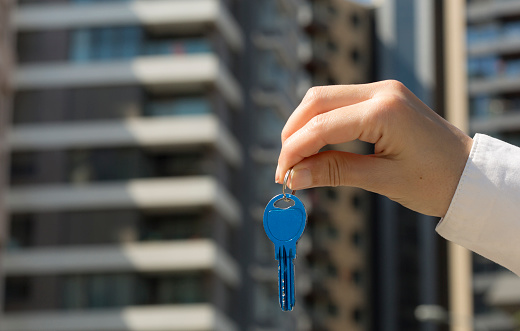 Hand showing a key. Buildings and city in background. Real estate concept.