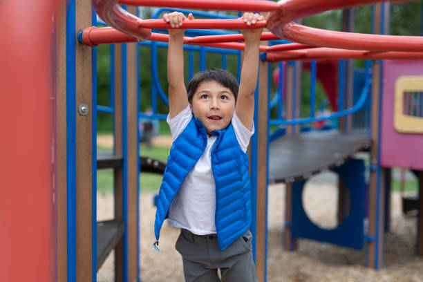 istock Young boy hanging from a play structure at the playground 1159292114