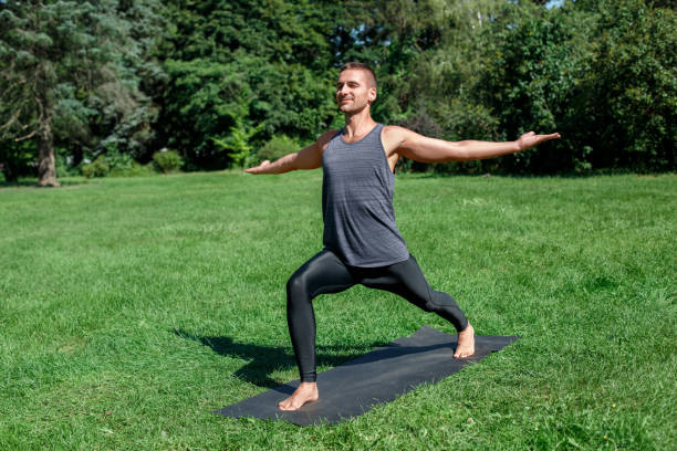 istock Healthy Lifestyle. Man practicing yogaon mat outdoors in warrior pose hands aside joyful 1159292401
