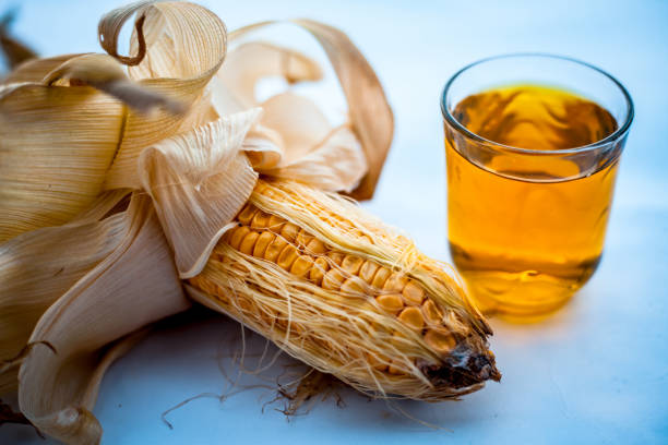 Raw organic fresh corn cob isolated on white along with its extracted fresh extract in a glass.