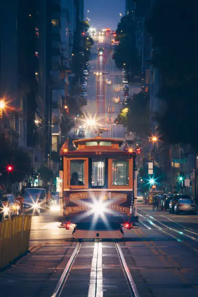 Classic view of historic traditional Cable Cars riding on famous California Street at night with city lights, San Francisco, California, USA