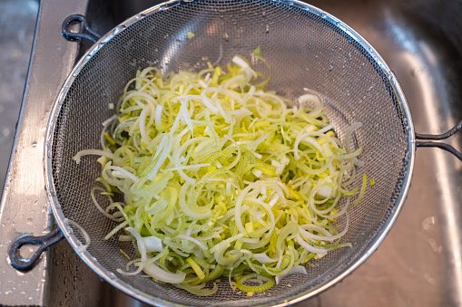 Thin slices of leek are put into a strainer to wash off the dirt prior to cooking in soup.