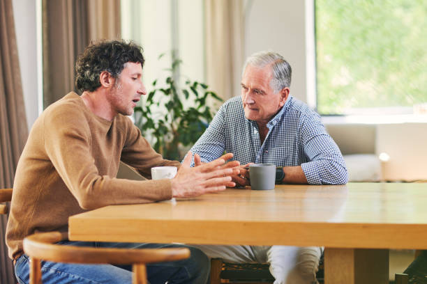 Visit your parents, they love to see you Shot of a mature man and his elderly father having coffee and a chat at home adult offspring stock pictures, royalty-free photos & images