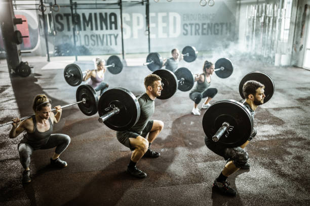 Group of athletes exercising deadlift with barbells in a health club. Large group of athletes making an effort while crouching with barbells in a gym. Barbell stock pictures, royalty-free photos & images