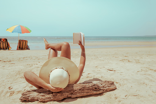 Leisure in summer - Young woman in straw hat lying sunbathe on a tropical beach, relax with book. Memories of summer vacation concept. retro color tone.