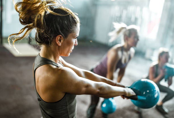 mujer atlética haciendo ejercicio con campana de hervidor en una clase en un club de salud. - deporte y salud fotografías e imágenes de stock