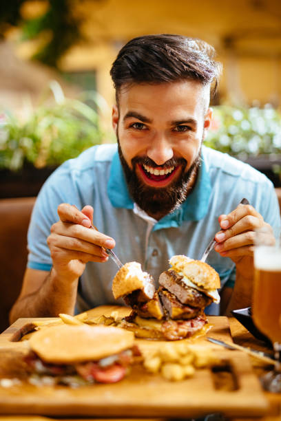 Portrait of a young man eating oversized burger in a fast food restaurant stock photo