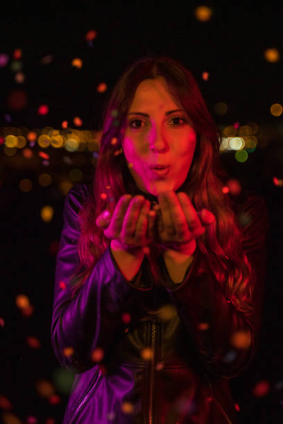 istock Young woman blowing confetti at night party 1159335717