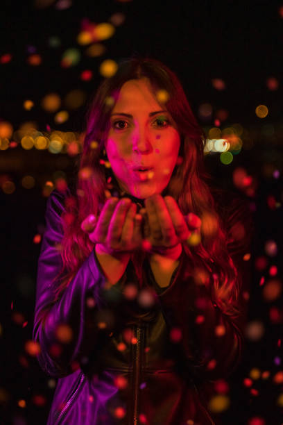 istock Young woman blowing confetti at night party 1159335720