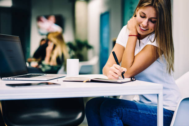 istock Cheerful young woman concentrated on writing article in notebook publicating on web page satisfied with freelance job, clever smiling female student prepare homework in campus with wifi and netbook 1159338327