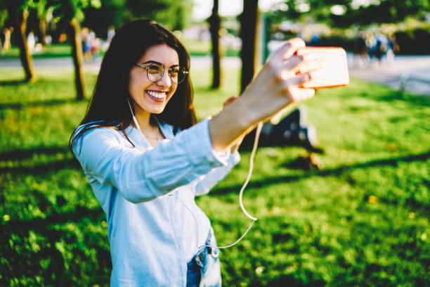 istock Happy female student posing for making selfie on smartphone camera satisfied with recreation, cheerful hipster girl taking picture via mobile during rest in park on sunny day for share in networks 1159339405
