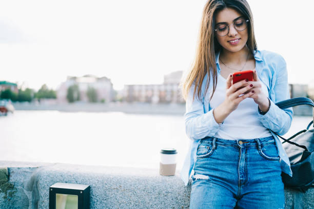 istock Young smiling woman in spectacles using telephone for networking while resting on free time in town, female tourist blogging using mobile phone  and 4G internet having sightseeing tour in town 1159339737