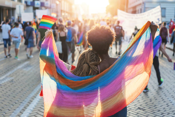 Multicultural female couple walking with the pride festival in Sofia Rear view image of multi-ethnic female couple embracing with colorful scarf and walking at the pride parade lgbtqcollection stock pictures, royalty-free photos & images