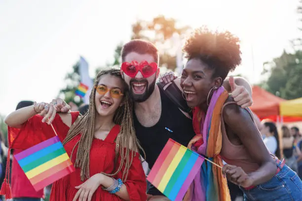 Young beautiful people celebrating the pride event, hugging, waving rainbow pride flags and having fun