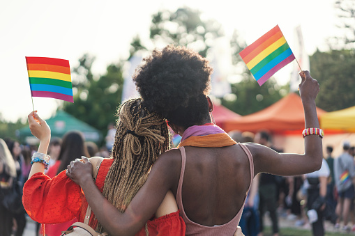 Rear view image of multi-ethnic female couple embracing and waving rainbow flag at the pride parade