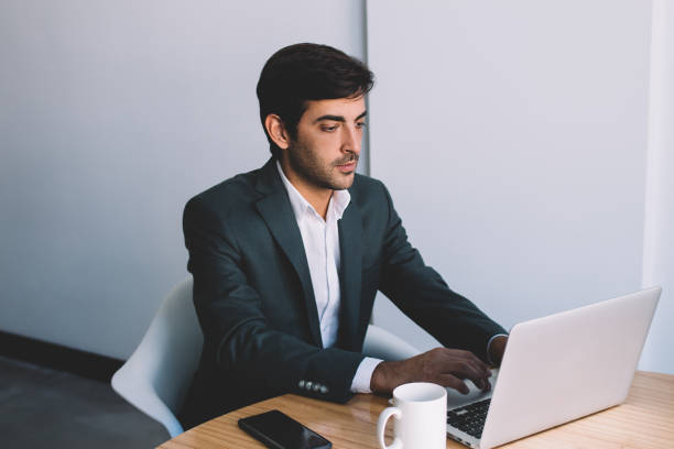 istock Indian businessman searching information and application for making productive presentation in corporate company using netbook at desktop, handsome guy wear in formal suit jacket reading news online 1159342327