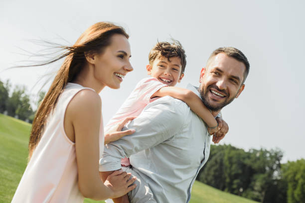 I love my parents! Young and strong father carrying his happy son on shoulders while spending time with family outdoors stock photo