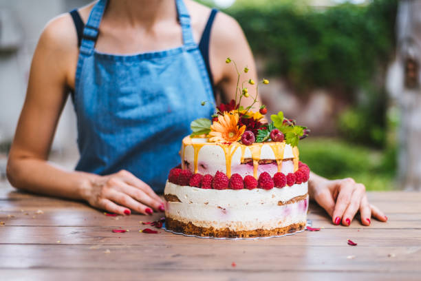Naked rustic cake with strawberries and white cream in front of young female  pastry-cook stock photo