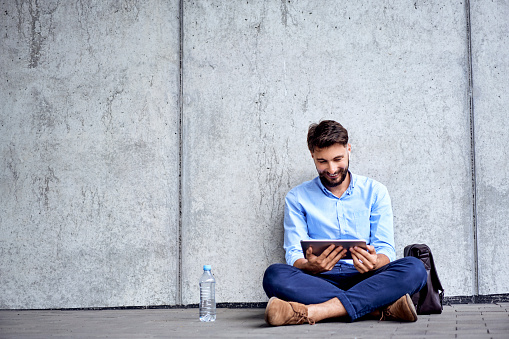 Young businessman sitting on ground in the city and looking at tablet