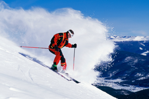 Man Snow Skiing in Front of Wave of Snow and Blue Sky
