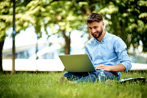 Portrait of young businessman sitting in the park and working on laptop