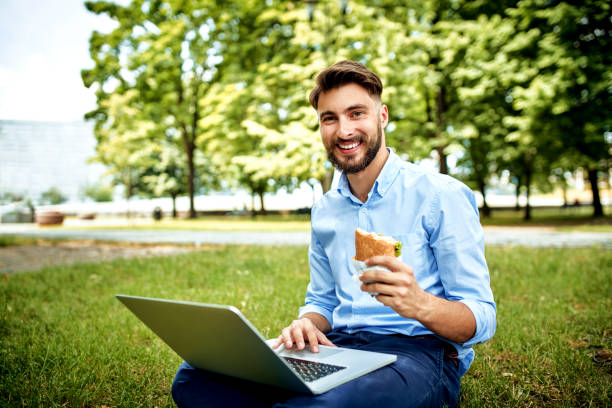 istock Cheerful young businessman looking at camera while having lunch and working in the park 1159351228
