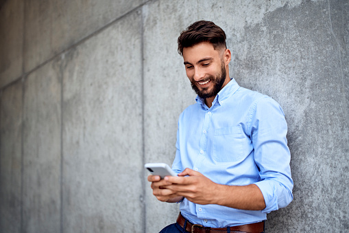 Young businessman smiling while texting on smartphone in the city