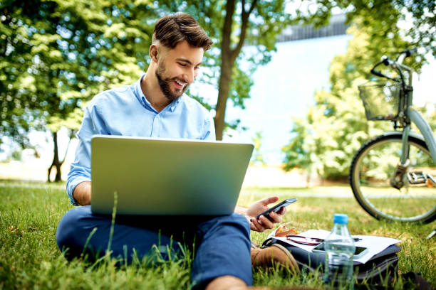 istock Happy young businessman using laptop and phone while sitting in the park during lunch break 1159352009