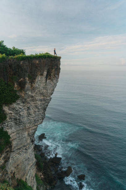 uomo in piedi sulla scogliera e guardando il mare a uluwatu, bali - cliffside foto e immagini stock