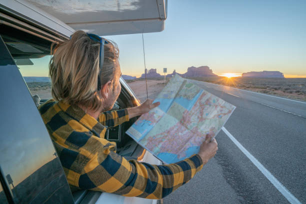 istock Road trip concept; Young man inside campervam looking at road map for directions exploring national parks and nature ready for adventure. 1159357586