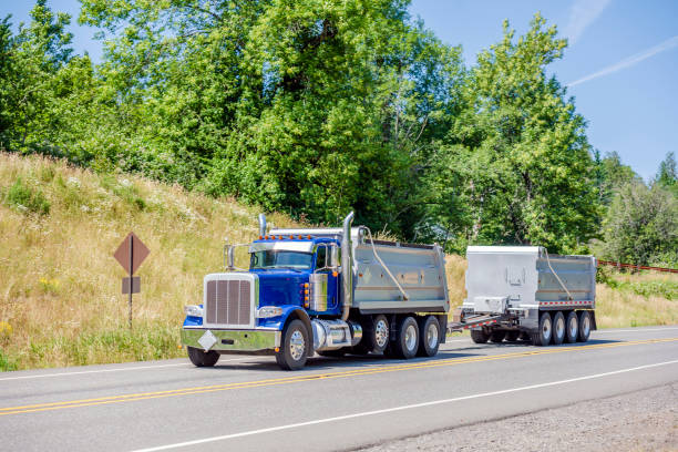 istock Blue big rig semi truck tipper with two tip trailers going on the road with hill 1159358086