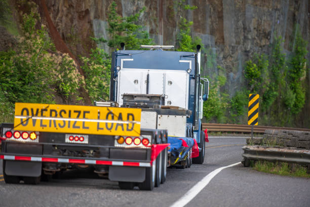 grande carro semi-camion con segno carico oversize dietro letto piatto semirimorchio che guida sulla strada di montagna con parete rocciosa sul lato - oversized foto e immagini stock