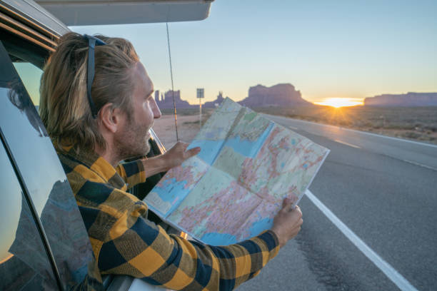 istock Road trip concept; Young man inside campervam looking at road map for directions exploring national parks and nature ready for adventure. 1159360399