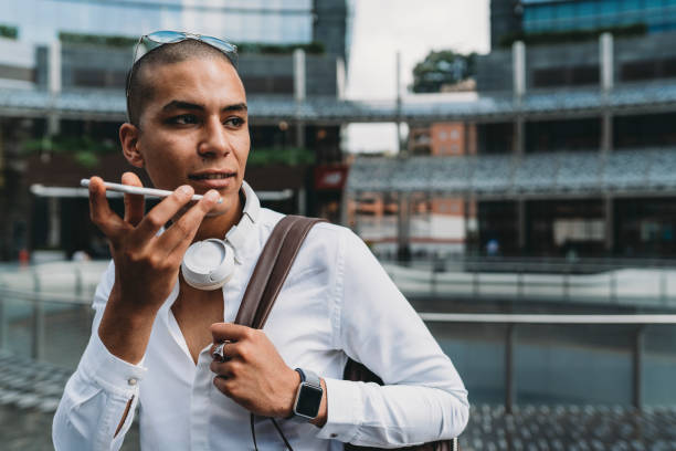 young adult businessman sending a voicemail with smartphone in the city - conference phone imagens e fotografias de stock