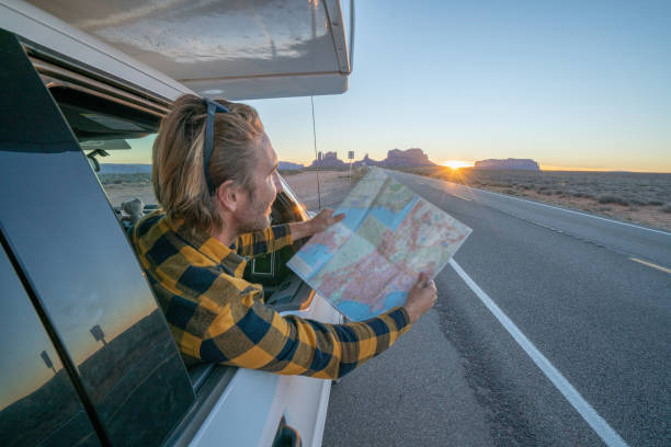 istock Road trip concept; Young man inside campervam looking at road map for directions exploring national parks and nature ready for adventure. 1159360741