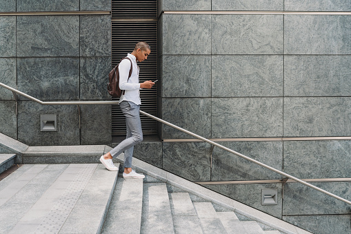 Young adult businessman in the city going down the stairs with smart phone