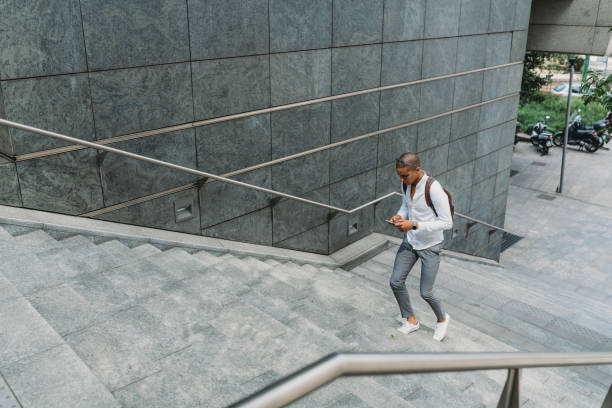 giovane uomo d'affari adulto in città salendo le scale con lo smartphone - scala milano foto e immagini stock