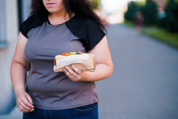 overweight woman eating fast-food walking outdoors - eating sandwich emotional stress food imagens e fotografias de stock