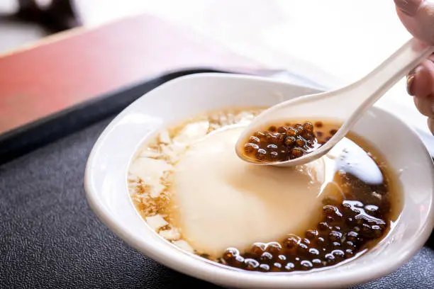 Photo of Popular Taiwan gourmet - Dessert of tapioca pearl ball (bubble) mixed bean curd tofu pudding (douhua, dou hua) in white bowl, close up, lifestyle