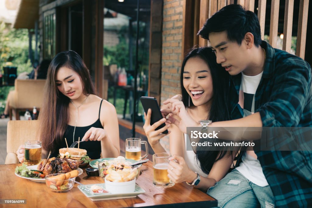 Asian single woman envious with love couple doing take selfie at restaurant. Former Stock Photo
