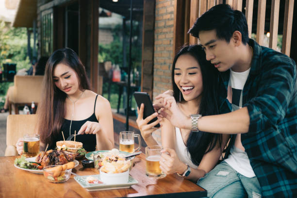 asian single woman envious with love couple doing take selfie at restaurant. - former imagens e fotografias de stock