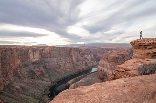 View of a girl looking at the famous horseshoe bend by the Colorado river at sunset, beautiful dramatic colourful sky. people travel concept