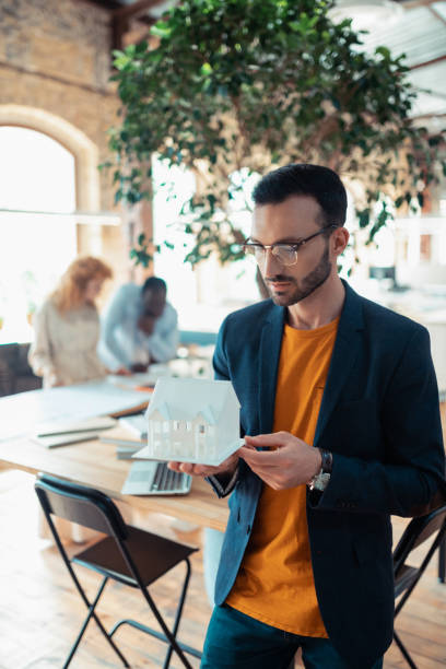istock Handsome dark-haired man holding white model of house 1159365561