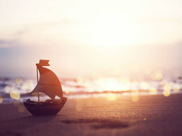 istock Silhouette small boat toy on sand at sunset beach 1159365740